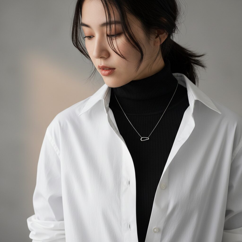 白シャツのボタンを少し開け、中に黒の薄手タートルネックを重ね着したレイヤードスタイルのクローズアップ。コットンとニットの異素材感が際立つ。